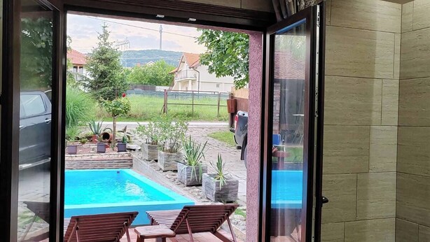 Una puerta corrediza de vidrio da a un área de piscina con dos sillas de madera y una mesita.