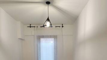 Una habitación pequeña y limpia, con una cama individual, una ventana con cortina translúcida y una lámpara colgante.