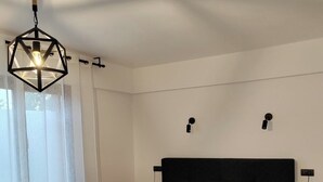 Un dormitorio moderno con una cama grande, una lámpara colgante de diseño y vistas al exterior a través de cortinas translúcidas.