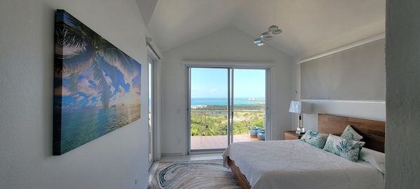 A bedroom with a large painting, a bed with a wooden headboard, a nightstand, and a view through a sliding glass door.