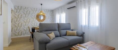 A modern living room with a grey sofa, a wooden coffee table, and a wicker pendant light.