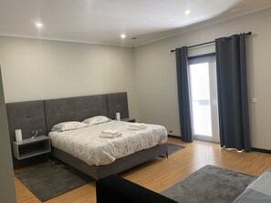 Ein modernes Schlafzimmer mit einem großen Bett, Nachttischen, einem Fenster mit Vorhängen und Blick ins Freie.