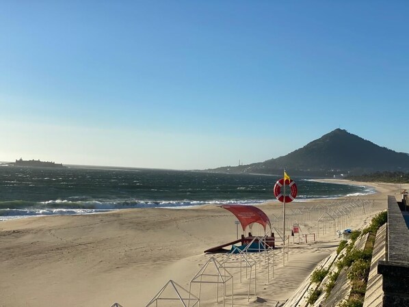 Ein Strand mit einem Rettungsturm, einer Flagge und einem Berg im Hintergrund.