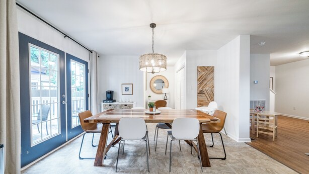 A modern dining area with a large wooden table, white chairs, and a hanging light fixture.