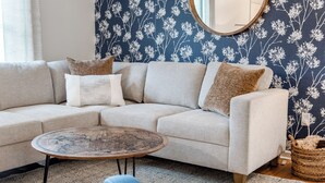 A living room with a beige sectional sofa, a round coffee table with a map design, a woven basket, and a wall with a floral pattern.
