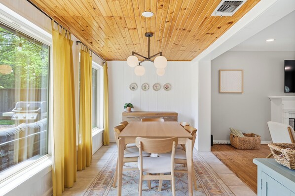 A dining area with a wooden ceiling, a table with chairs, a television, and a fireplace.
