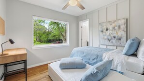 A bedroom with a bed, a desk, a window, a ceiling fan, and a painting. - Modern & Cozy 3BR near UTA/AT&T (Arlington)