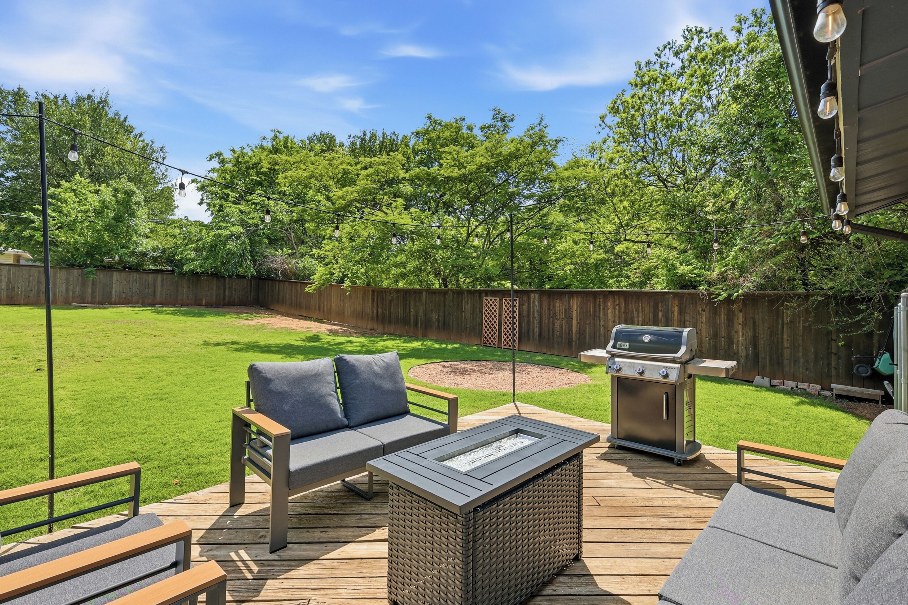 A backyard with a wooden deck, outdoor furniture, a grill, and a fire pit.