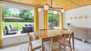 A dining area with a wooden table and chairs, large windows with curtains, and a view of a backyard. - Modern & Cozy 3BR near UTA/AT&T (Arlington)
