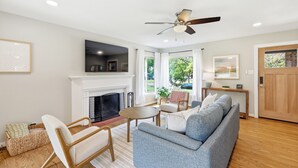A living room with a fireplace, a ceiling fan, and a view of the outdoors. - Modern & Cozy 3BR near UTA/AT&T (Arlington)