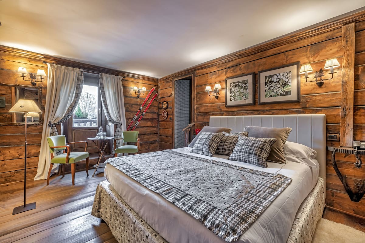 A cozy log cabin bedroom with a large bed, a chair, a small table, and a window with curtains.