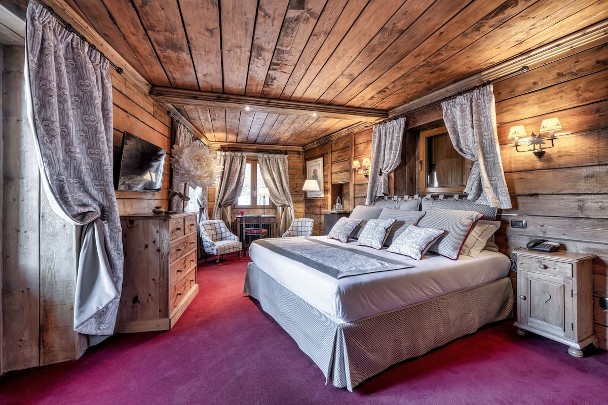 A wooden cabin bedroom with a large bed, two bedside tables, a dresser, and a mirror.
