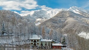 A snow-covered mountain landscape with a traditional chalet-style building featuring multiple windows and a red roof. - Chalet Bragard - Boutique Chalet & Spa (Limone Piemonte)