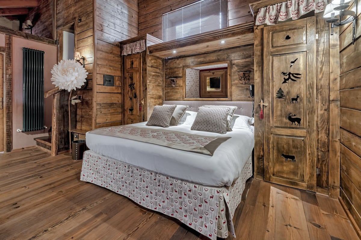 A wooden cabin-style bedroom with a large bed, a dresser, and a mirror.