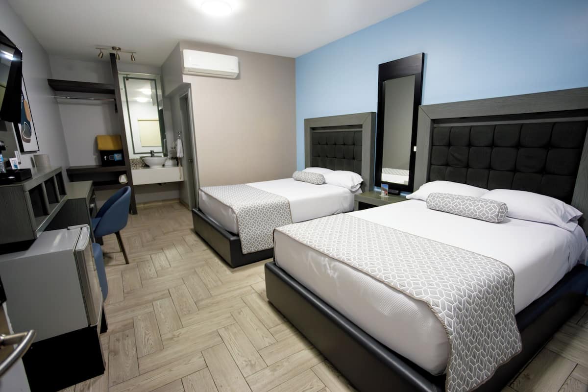 Une chambre d’hôtel avec deux lits, un bureau, une chaise, un miroir et un téléviseur.