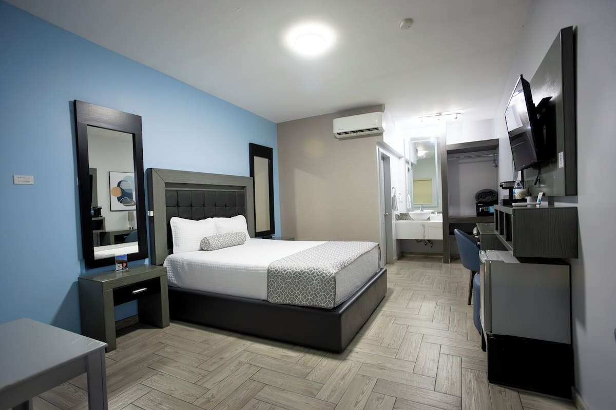 Une chambre d’hôtel moderne équipée d’un lit, de tables de chevet, d’un bureau, d’une chaise, d’un téléviseur et d’un appareil de climatisation.