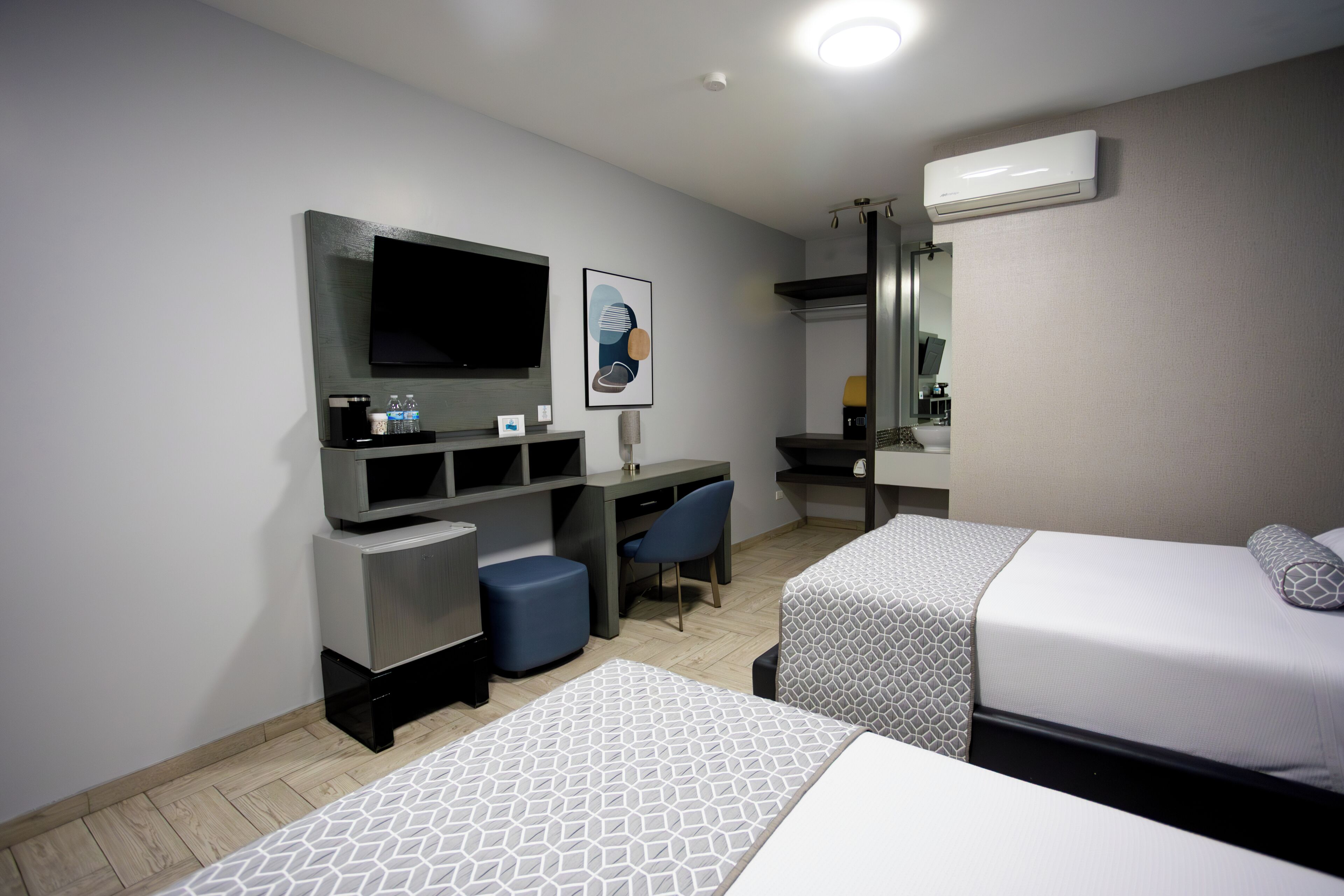 Habitación de hotel con dos camas, un escritorio con silla, un televisor de pantalla plana, un espejo y un equipo de aire acondicionado.