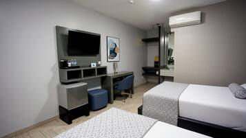 A hotel room with two beds, a desk with a chair, a flat-screen TV, a mirror, and an air conditioning unit.