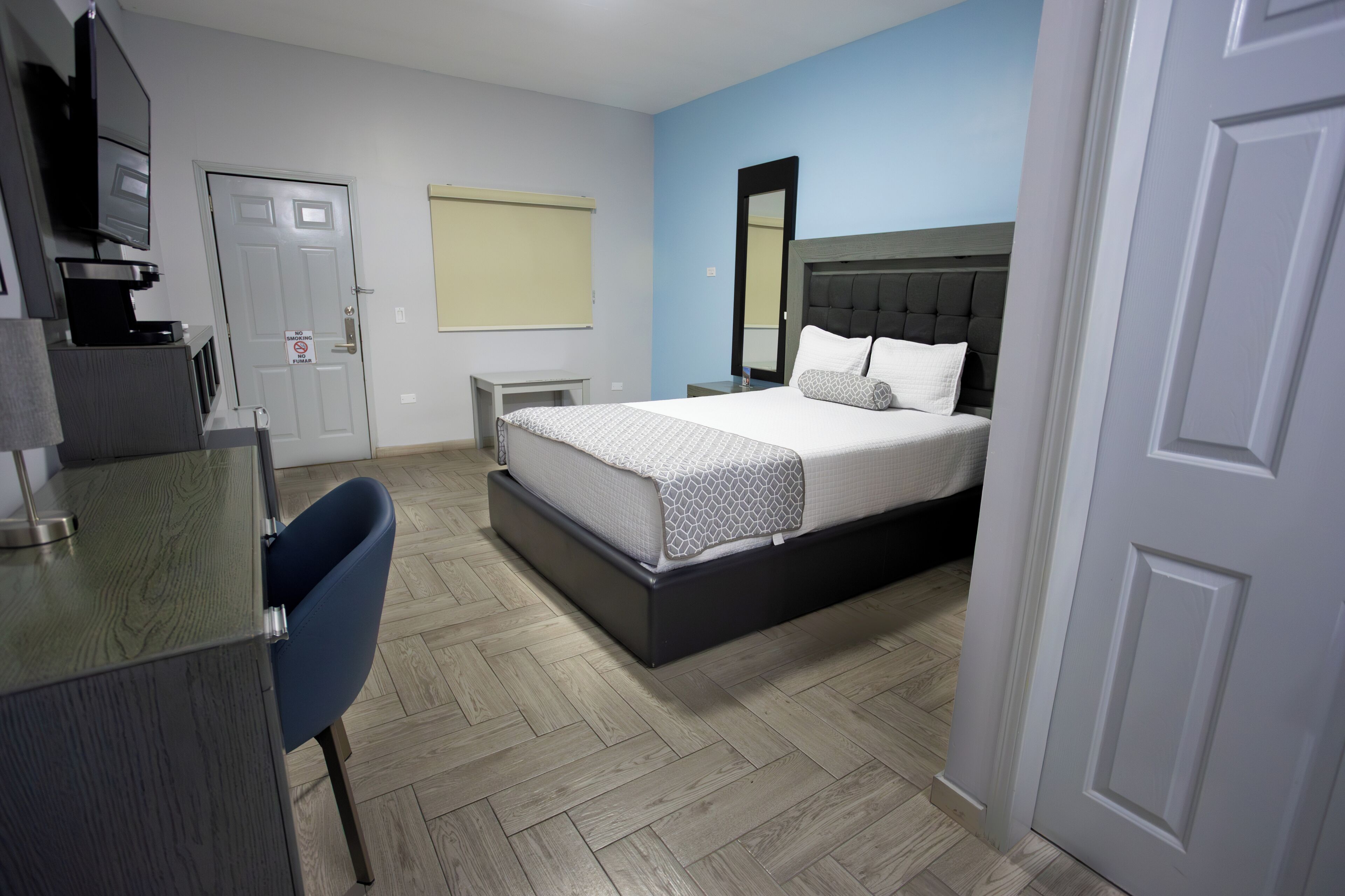 A hotel room with a bed, a desk, a chair, a TV, and a door.