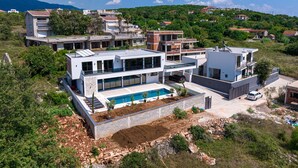 A modern two-story house with a swimming pool, surrounded by greenery and other residential buildings.