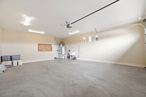 A spacious garage with a concrete floor, a ceiling-mounted projector, and a white wall with a small window.