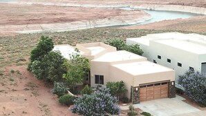 Une maison moderne avec un garage, entourée de végétation désertique et avec un grand plan d’eau en arrière-plan.