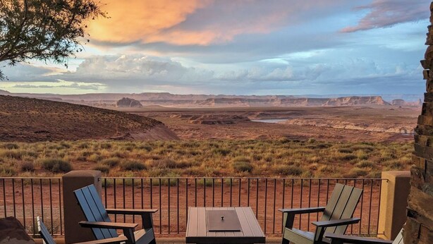 Une terrasse dotée de chaises Adirondack et d’une table, offrant une vue sur un paysage désertique avec des collines à l’horizon.
