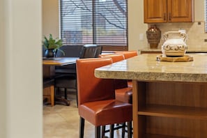 A kitchen with a granite countertop, wooden cabinets, a dining table with chairs, and a window with blinds.