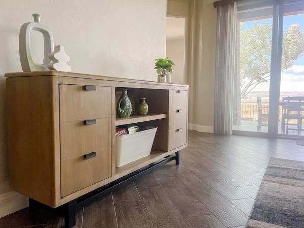 A wooden cabinet with drawers and shelves, a plant on top, and a window with a view of trees.