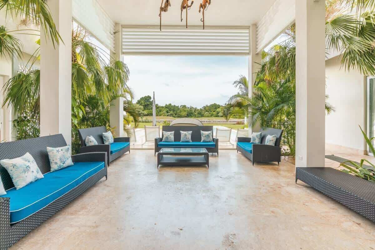 A covered outdoor seating area with sofas and a coffee table, surrounded by palm trees and a view of the landscape.