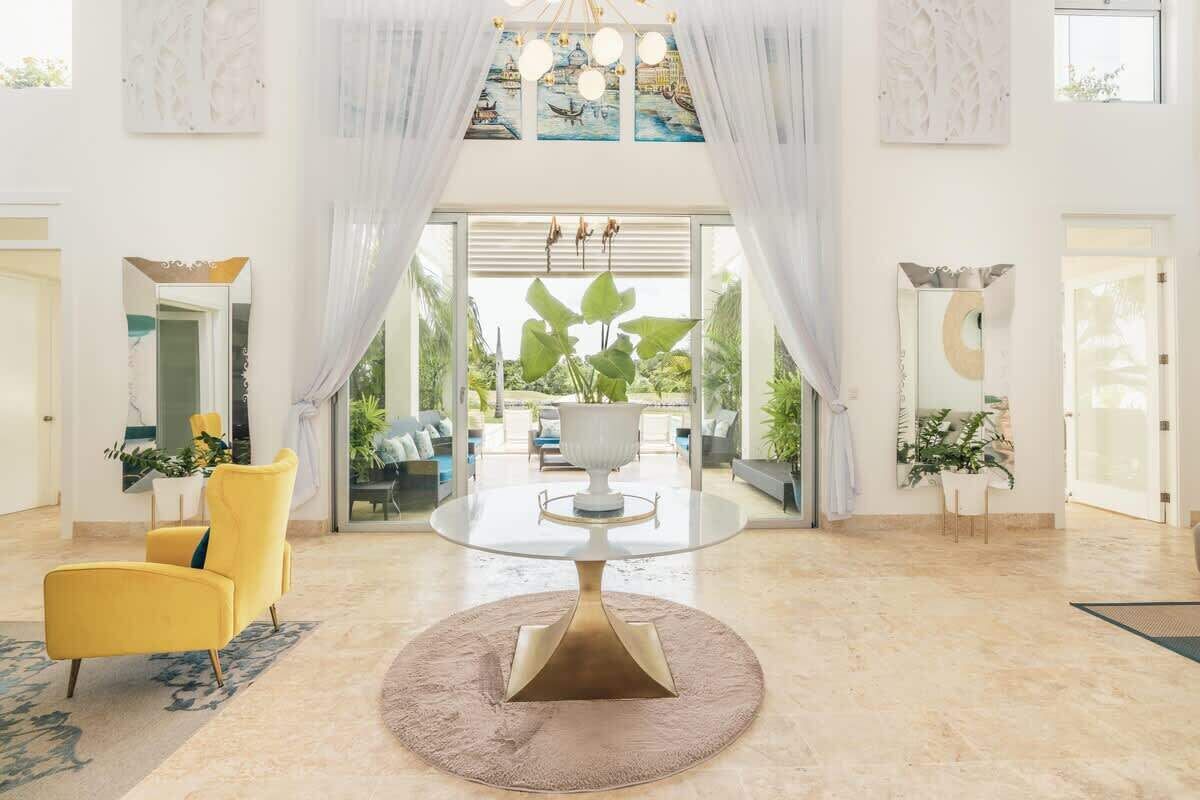 A spacious lobby with a round table, yellow armchairs, and a large window offering a view of the outdoors.