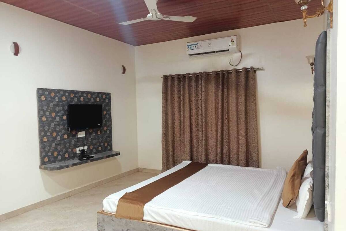 A bedroom with a bed, a flat-screen TV mounted on a patterned wall, a ceiling fan, and an air conditioning unit.