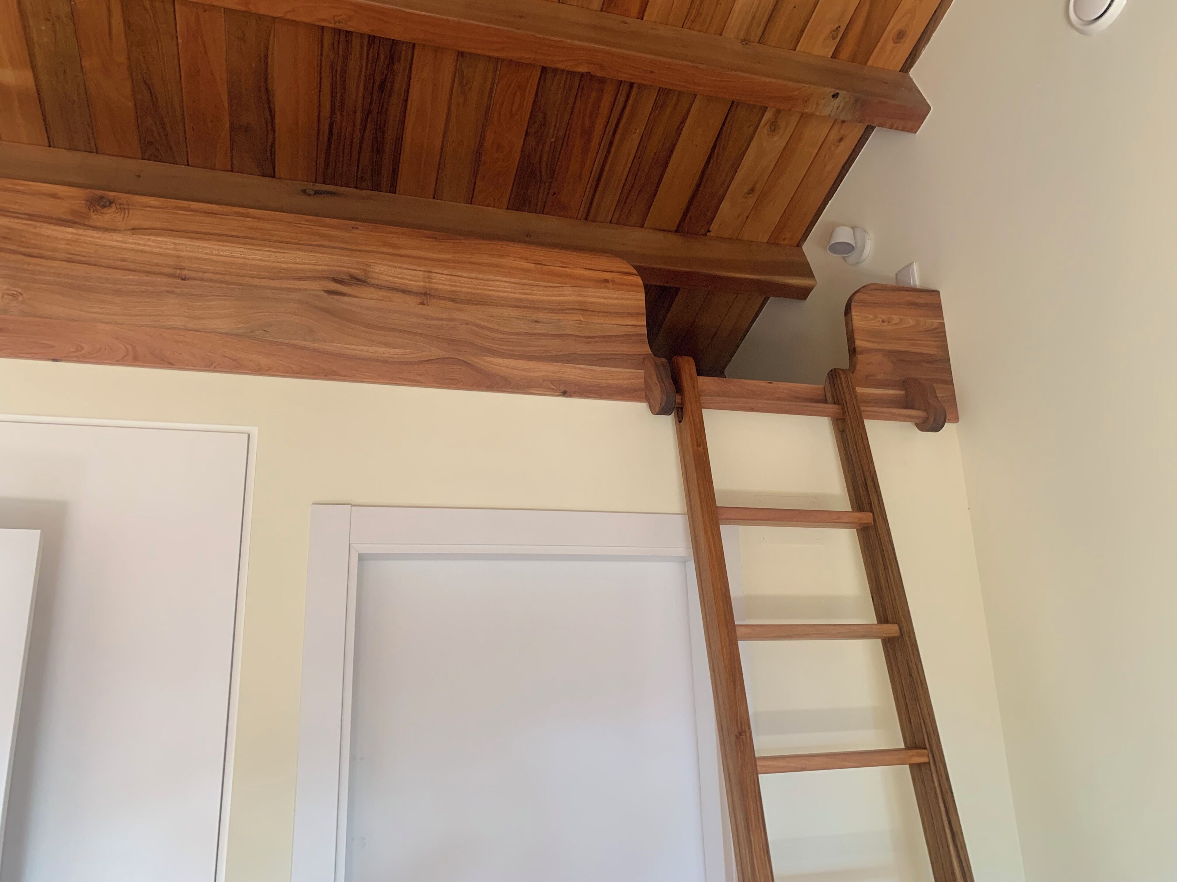 Techo de madera con una escalera de madera apoyada contra una puerta blanca.