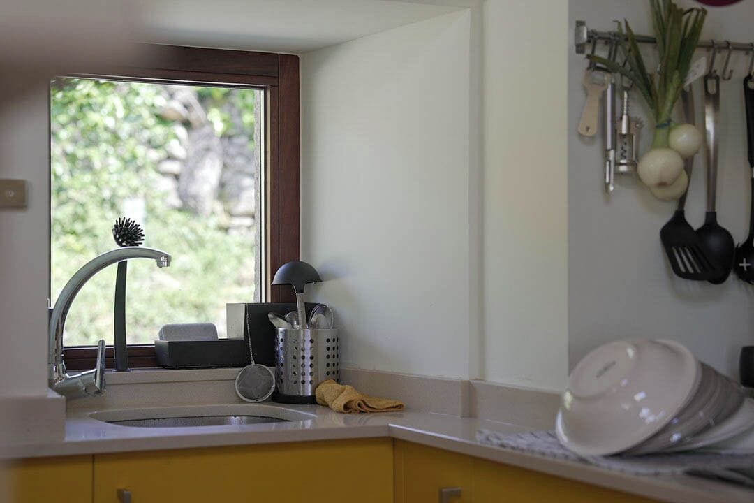 Una cocina con ventana, un lavamanos y diversos utensilios colgados en la pared.