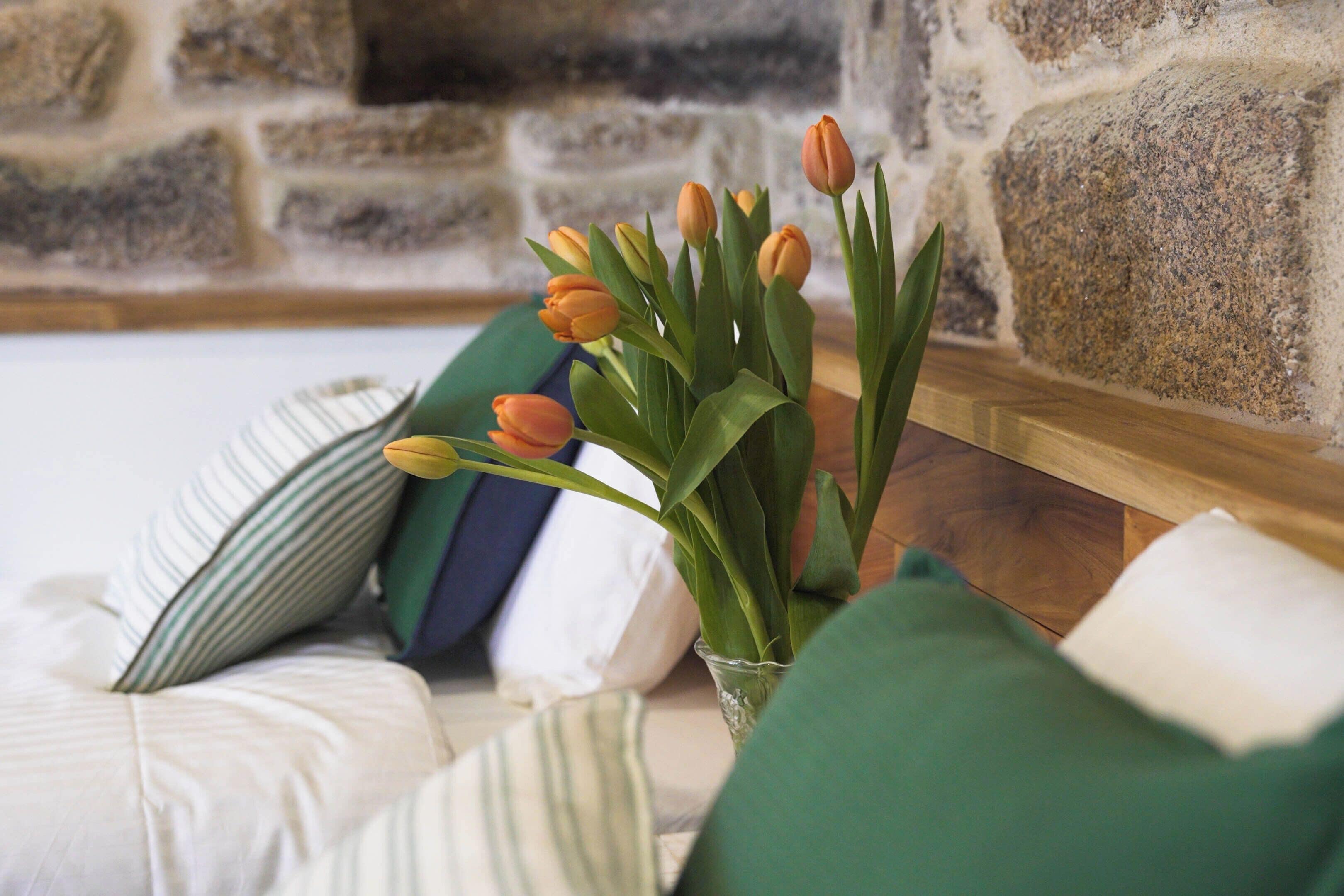 A bed with a vase of orange tulips, green pillows, and a stone wall in the background.