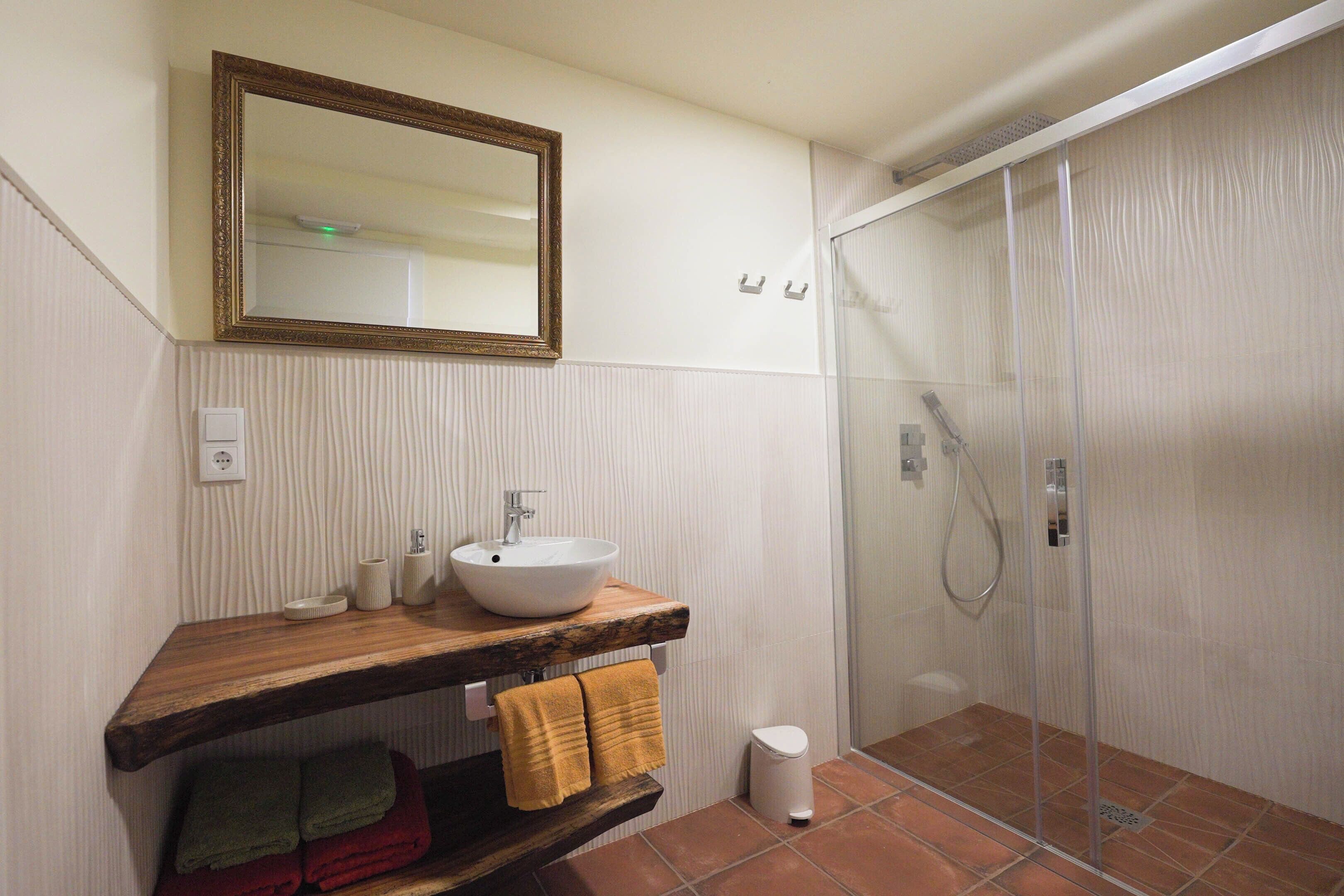 A bathroom with a wooden vanity, a white sink, a mirror, and a glass shower enclosure.