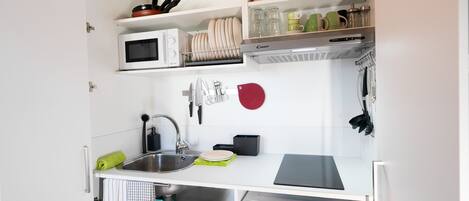 A compact kitchen with a microwave, sink, and various utensils.