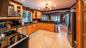 A spacious kitchen with wooden cabinets, a large island, stainless steel appliances, and a chandelier. - Lake Cottage | 5 Bed, 5 Bath (Lake Placid)