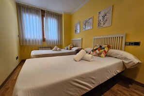A hotel room with two beds, a window with curtains, a radiator, and wall art.