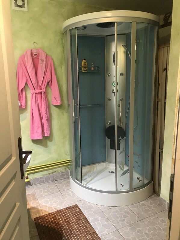 Une salle de bain avec une douche à parois de verre, un peignoir rose accroché au mur et un sol carrelé.