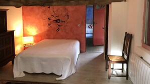 A bedroom with a bed, a chair, a lamp, and a red wall with a decorative design. - Plain Pied Dépendance Chez L'habitant (Bazancourt)