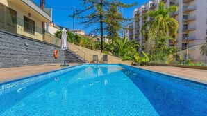 Una piscina con agua azul cristalina, rodeada por un muro de piedra y una terraza de madera.