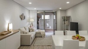 Una habitación moderna y luminosa con sofá, mesa de comedor y una silla colgante, además de una cesta de frutas.