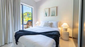 Une chambre d’hôtel avec un grand lit, deux lampes de chevet, une fenêtre avec des rideaux et deux tableaux encadrés accrochés au mur.