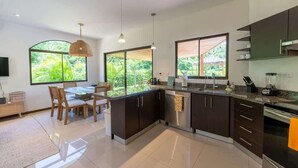 Une cuisine moderne avec des meubles de couleur sombre, un îlot central et de grandes fenêtres donnant sur un paysage verdoyant.