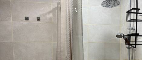 A shower with a glass door, a handheld showerhead, and a wall-mounted faucet.