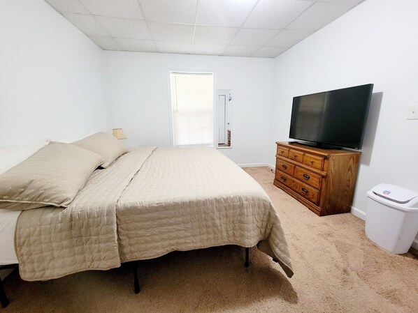 A bedroom with a bed, a dresser, a television, and a waste bin.