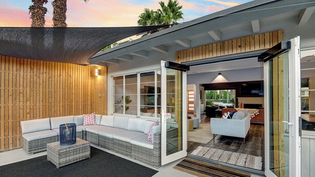 Una zona living esterna moderna con un divano, mobili in vimini e una porta vetrata che dà su un ambiente interno.