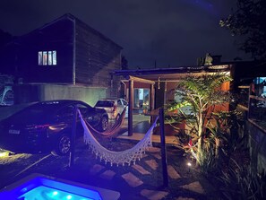 A residential area with a hammock, a car, and a house with a visible window. - Beach House with a Spa! Fire pit / Spa / Hammocks / Gardens / Parking lot (Morro das Pedras Florianópolis)