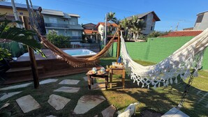 A hammock, a hot tub, and a dining table with food and drinks in a backyard. - Beachfront house with spa! Fire pit / Spa / Hammocks / Gardens / Parking (Morro das Pedras Florianópolis)